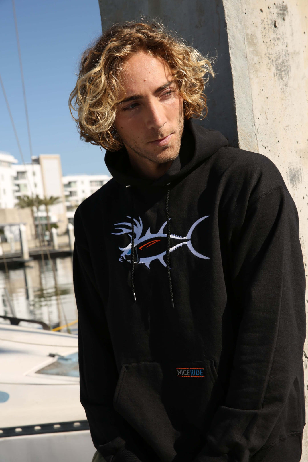 Young man wearing a black hoodie featuring a unique fish design by the water, perfect for hoodie season.