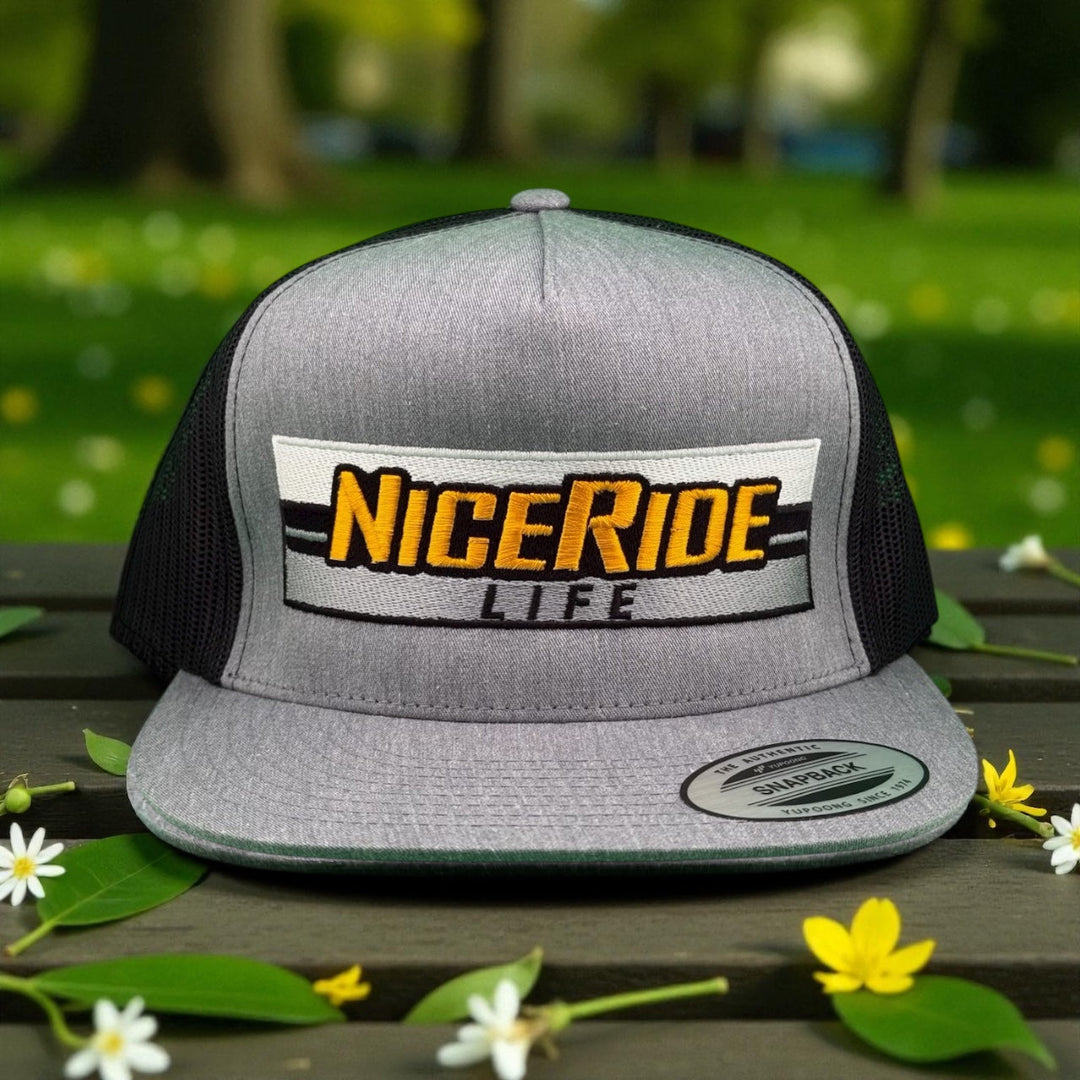 NiceRide Life snapback hat on a wooden table surrounded by flowers, perfect for stylish outdoor wear. Featuring Hat.