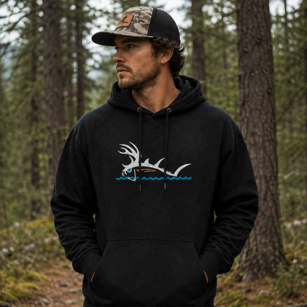 Man wearing NICERIDE black pullover hoodie featuring Buck-Eye Surface graphic in a forest setting.