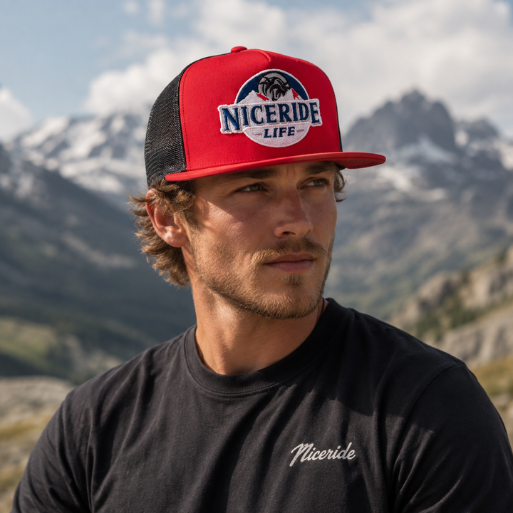 A man wearing the NICERIDE "Nice Ice" 6006 Classic Snapback Trucker Hat against a mountain backdrop, showcasing the hat.