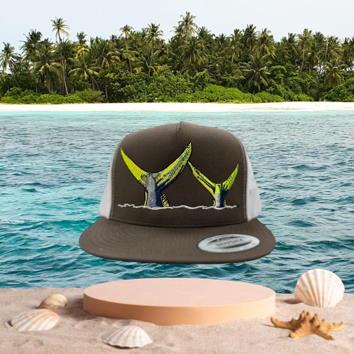NICERIDE Tall Tails snapback trucker hat with whale tail design against tropical beach backdrop.