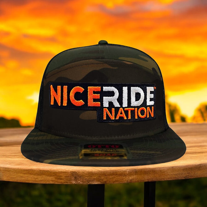 Camo NiceRide Nation cap displaying vibrant embroidered logo against a sunset backdrop.