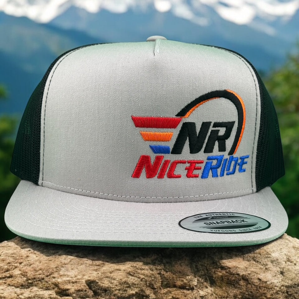 NICERIDE "REV" unisex trucker hat with embroidered logo on a scenic outdoor background.
