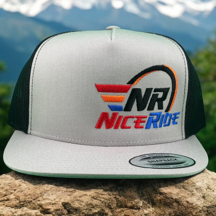 NICERIDE "REV" unisex trucker hat with embroidered logo on a scenic outdoor background.