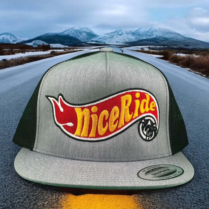NICERIDE Matchbox 6006 Trucker Hat on a scenic road, showcasing its classic snapback design and vibrant logo.
