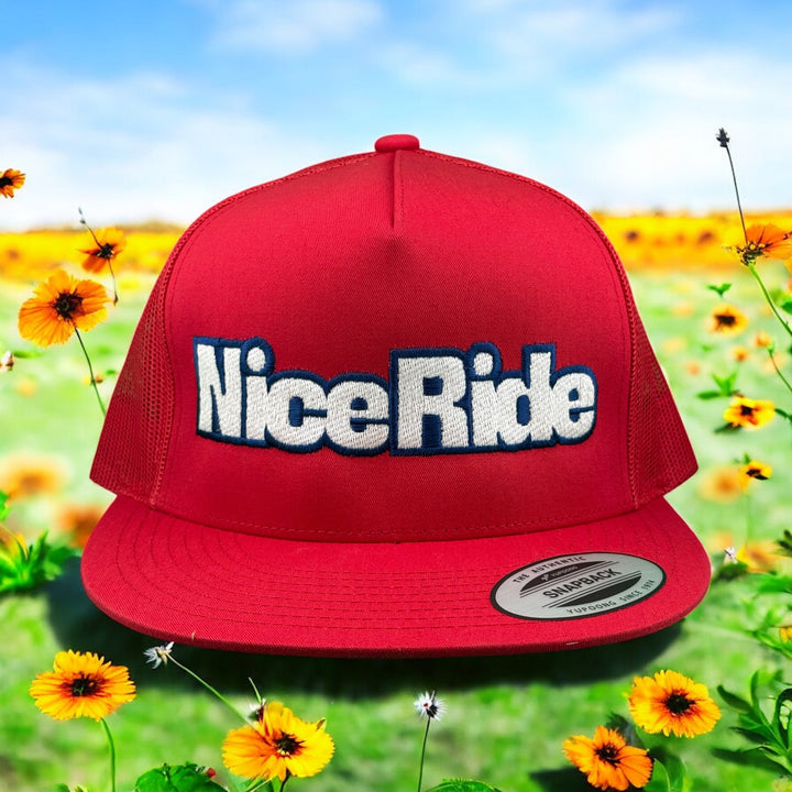 Red unisex adjustable trucker hat with "NiceRide" embroidery, set against a vibrant nature background.