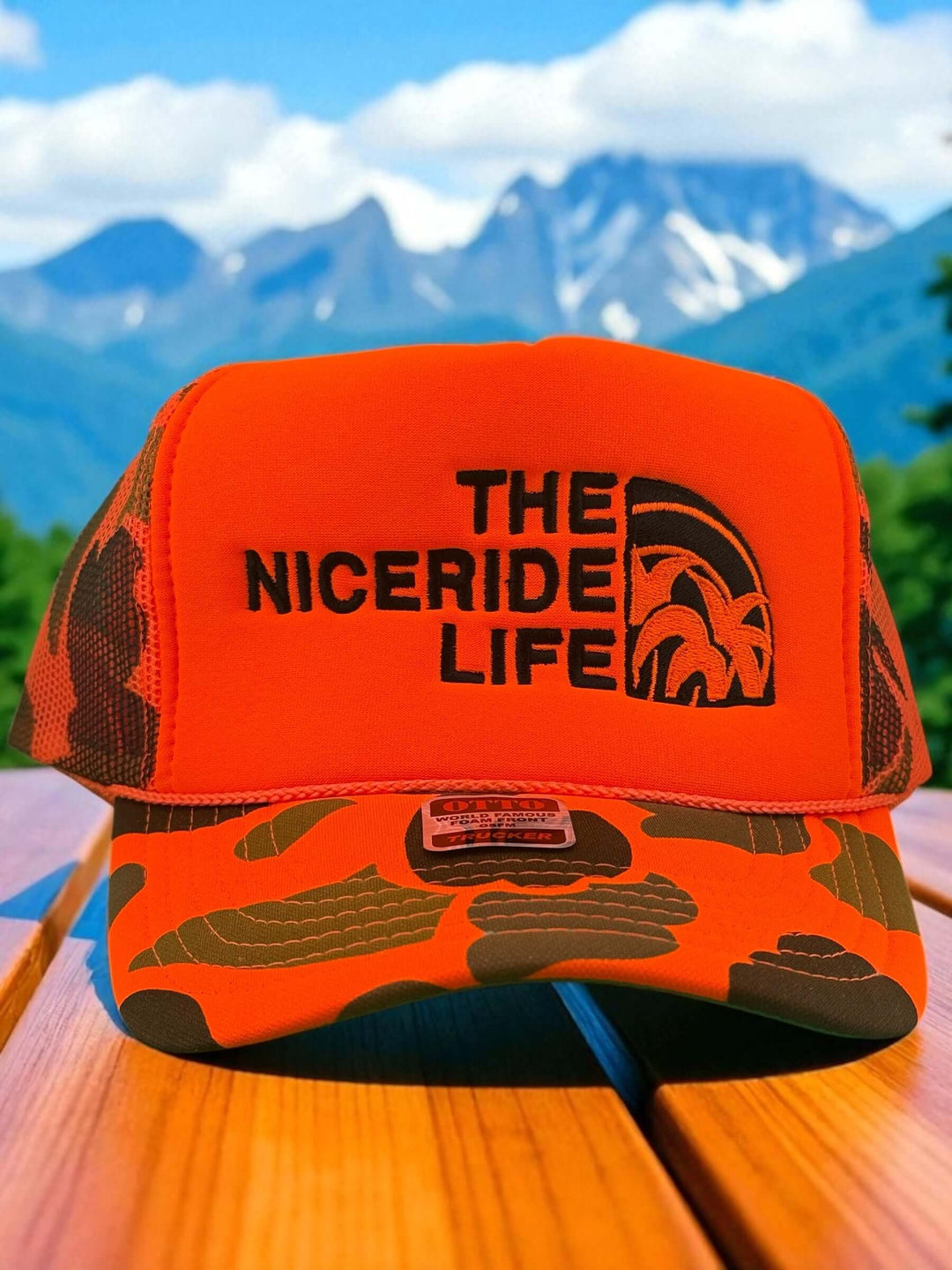NICERIDE Life orange foam trucker hat with camouflage design against a mountain backdrop.
