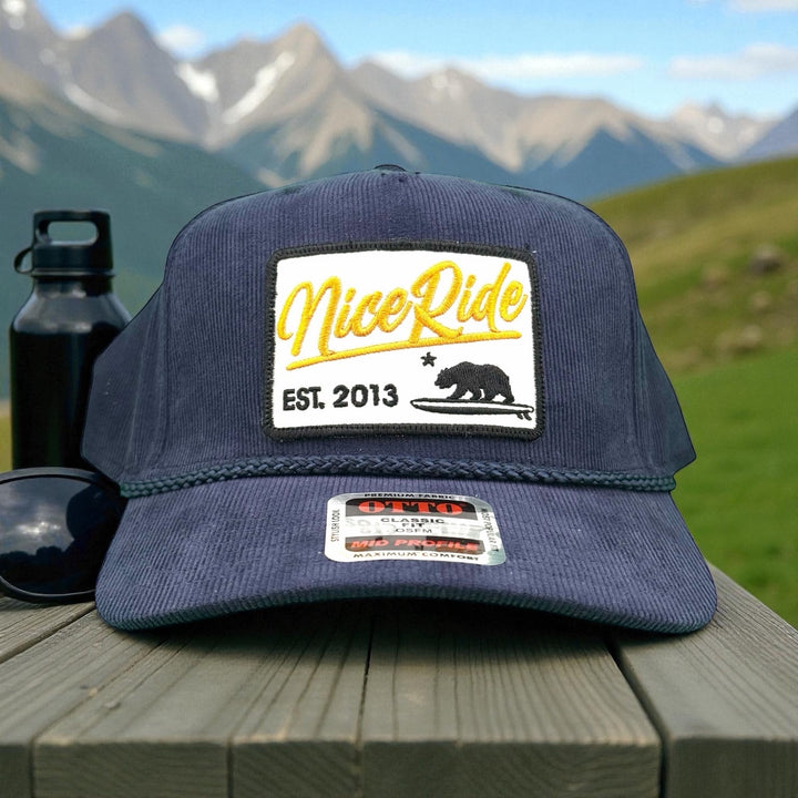 "Big Sky" corduroy snapback baseball cap with NiceRide logo against mountain backdrop.