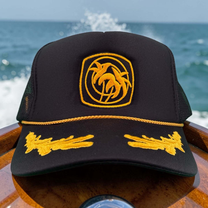 Below Deck Moe Doe hat on a boat with ocean in background, showcasing palm tree logo and vibrant colors.