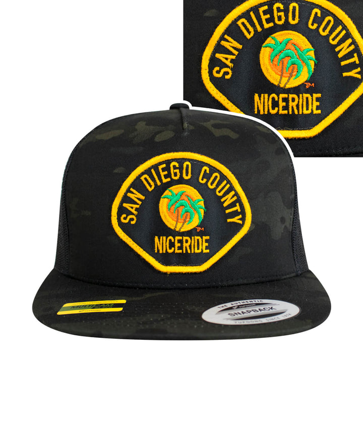 The Badge Trucker Hat with NICERIDE design, black camouflage cap featuring San Diego County embroidery.