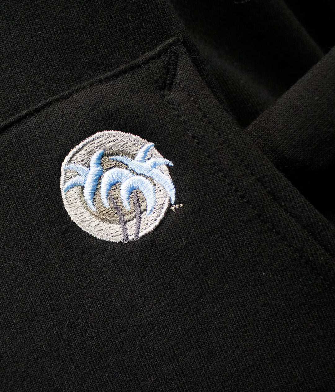 Close-up of NICERIDE palm logo embroidered on black pullover hoodie, showcasing quality craftsmanship.