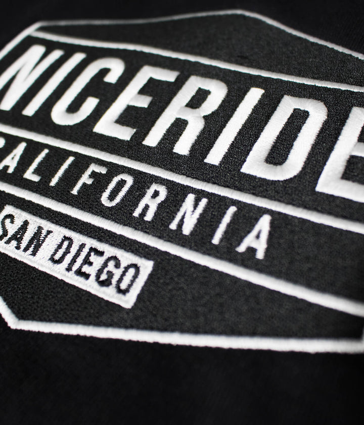 Close-up of NICERIDE California logo embroidered on black hoodie fabric.