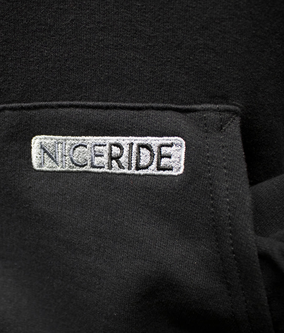 Close-up of NICERIDE logo embroidered on a black pullover hoodie, showcasing quality and style.