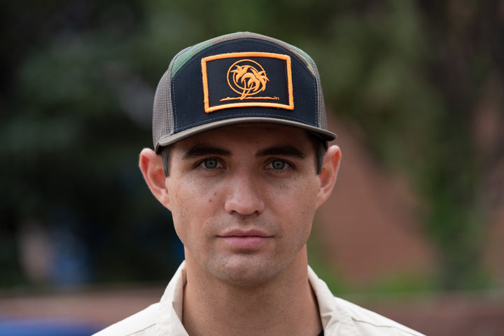 Man wearing a "Palm Patch" 7 Panel Trucker Snapback Cap, front view showcasing neon orange embroidery.