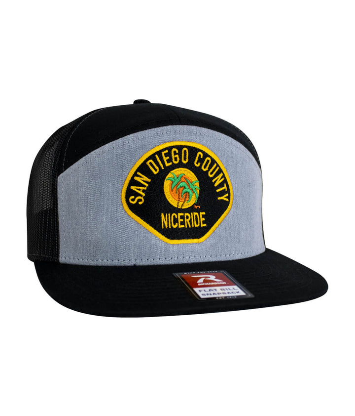 The Badge 7 Panel Trucker Hat featuring NICERIDE design and San Diego County embroidery.