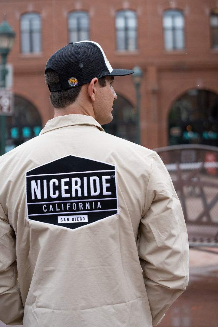 Man wearing a beige windbreaker jacket with NICERIDE logo on the back in San Diego.