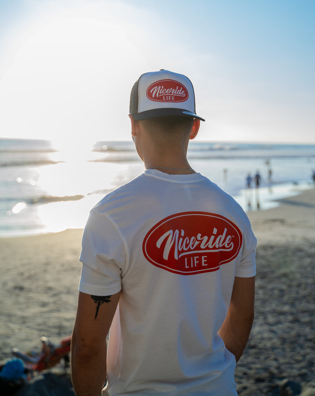 Man wearing a NiceRide Life shirt at the beach during sunset, showcasing quality cotton fabric.