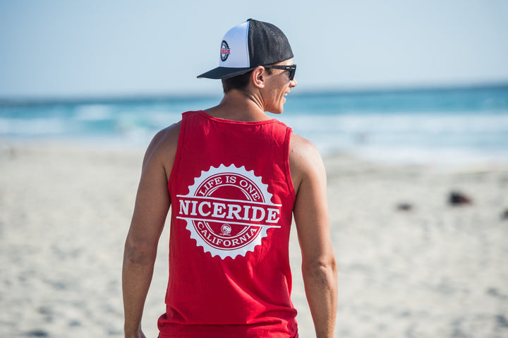 Man wearing a red tank top with NICERIDE logo at the beach, enjoying outdoor activity in summer.
