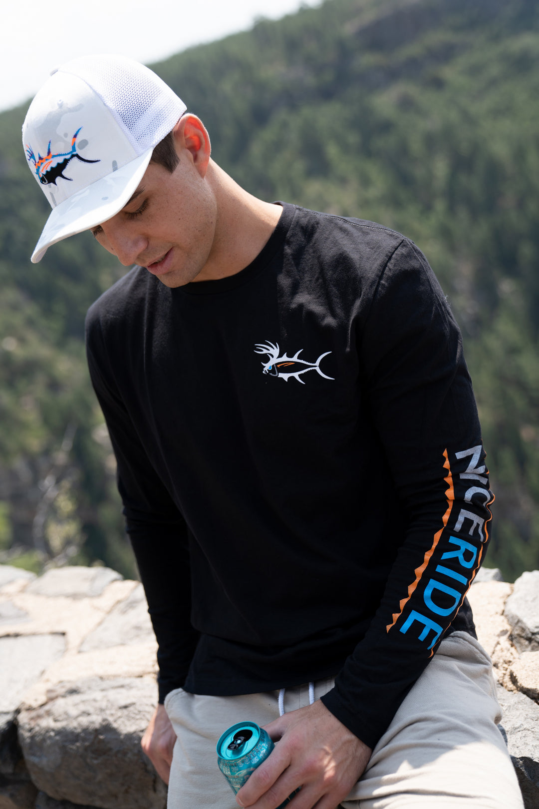 Man wearing a black long sleeve shirt with NICERIDE logo, outdoors with a scenery background.
