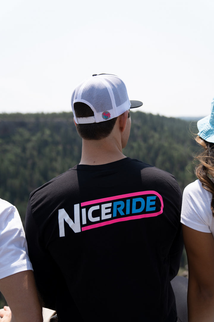 Man wearing The Tube black shirt with NICERIDE logo on back, outdoors with trees in background.