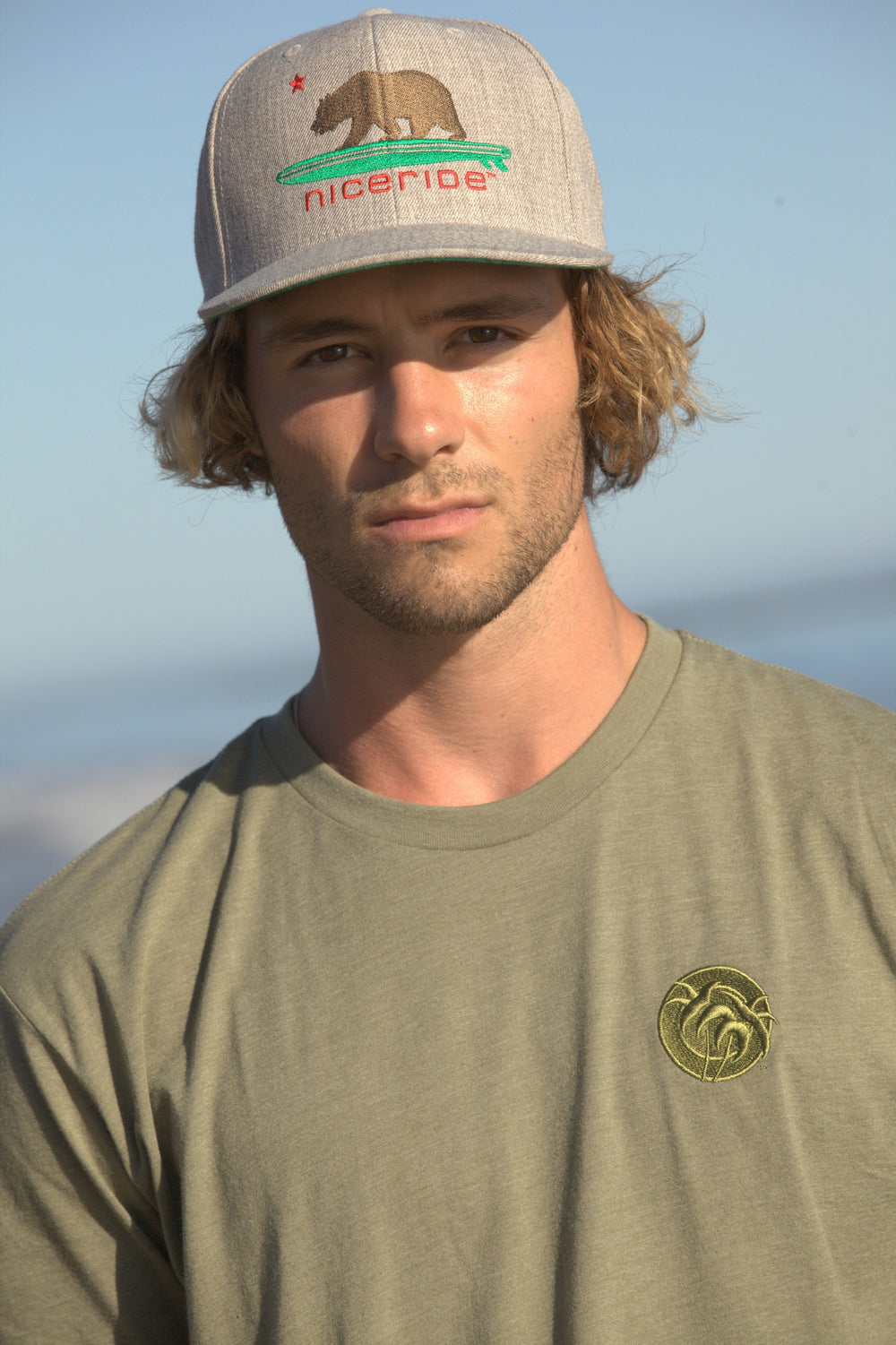 Man wearing a Tone Men's Next Level Short Sleeve Embroidered Shirt and NICERIDE cap on the beach.